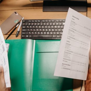 A person holding a balance sheet above their computer