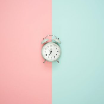 An alarm clock against a pink and blue background