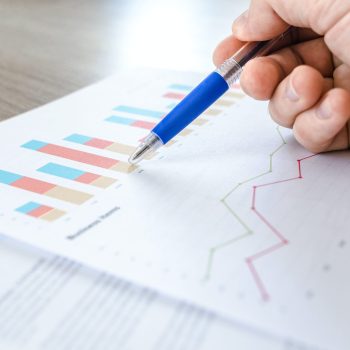 A person with a pen in hand looking over reporting documents