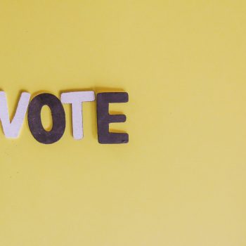 Pink and purple letters spelling "VOTE" against a yellow background